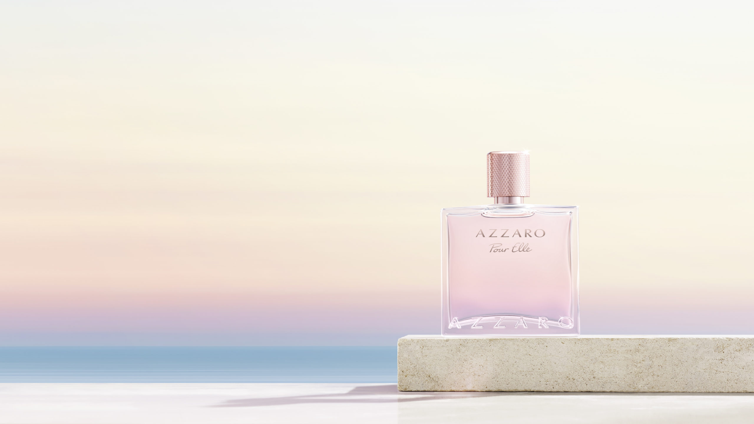Flacon du parfum Azzaro Pour Elle posé sur une pierre, avec en fond un ciel pastel et une mer calme, visuel élégant et lumineux.